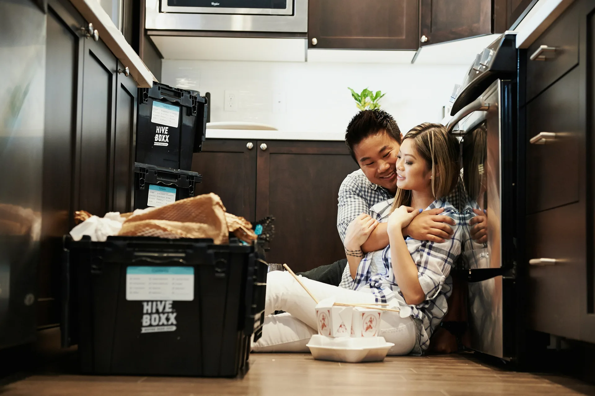 Couple relaxing on the kitchen floor beside their oven while unpacking in a new home