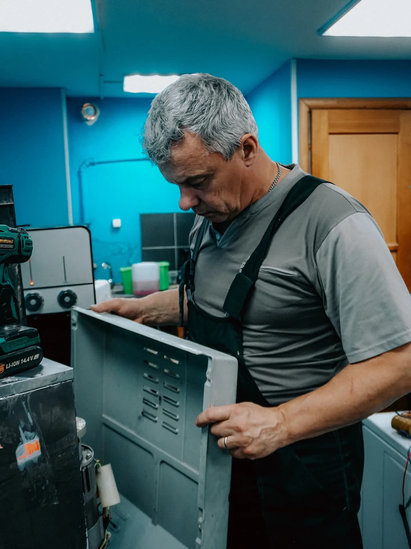 An experienced Appliance Repair Sherwood Park technician removes the vented back panel of an appliance in the workshop, showing the careful component-level diagnosis behind every chest and upright freezer repair.